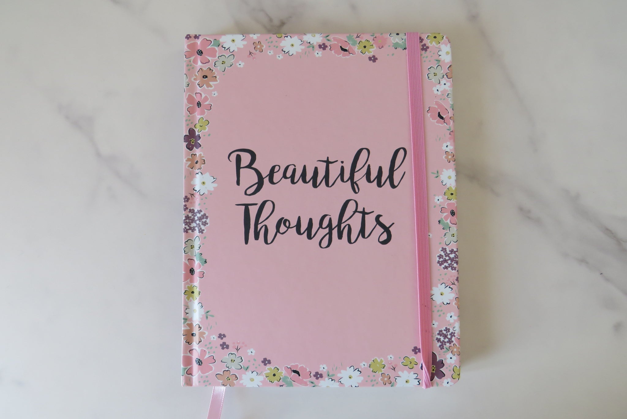 A pink notebook with 'Beautiful Thoughts' written on the cover, decorated with small floral designs around the border.
