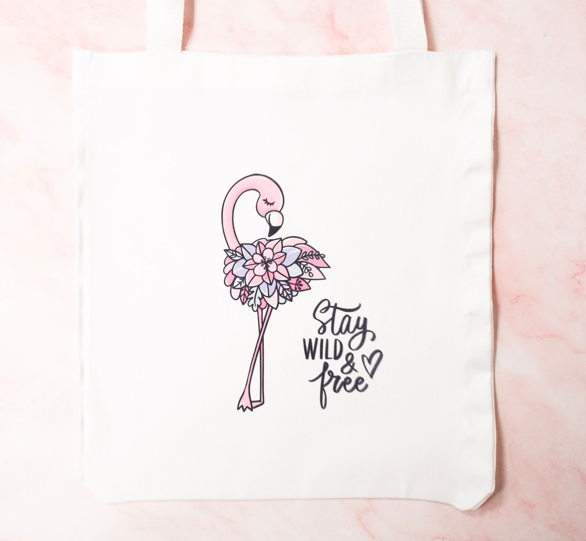 Floral flamingo design on a white tote bag with 'Stay Wild & Free' text.