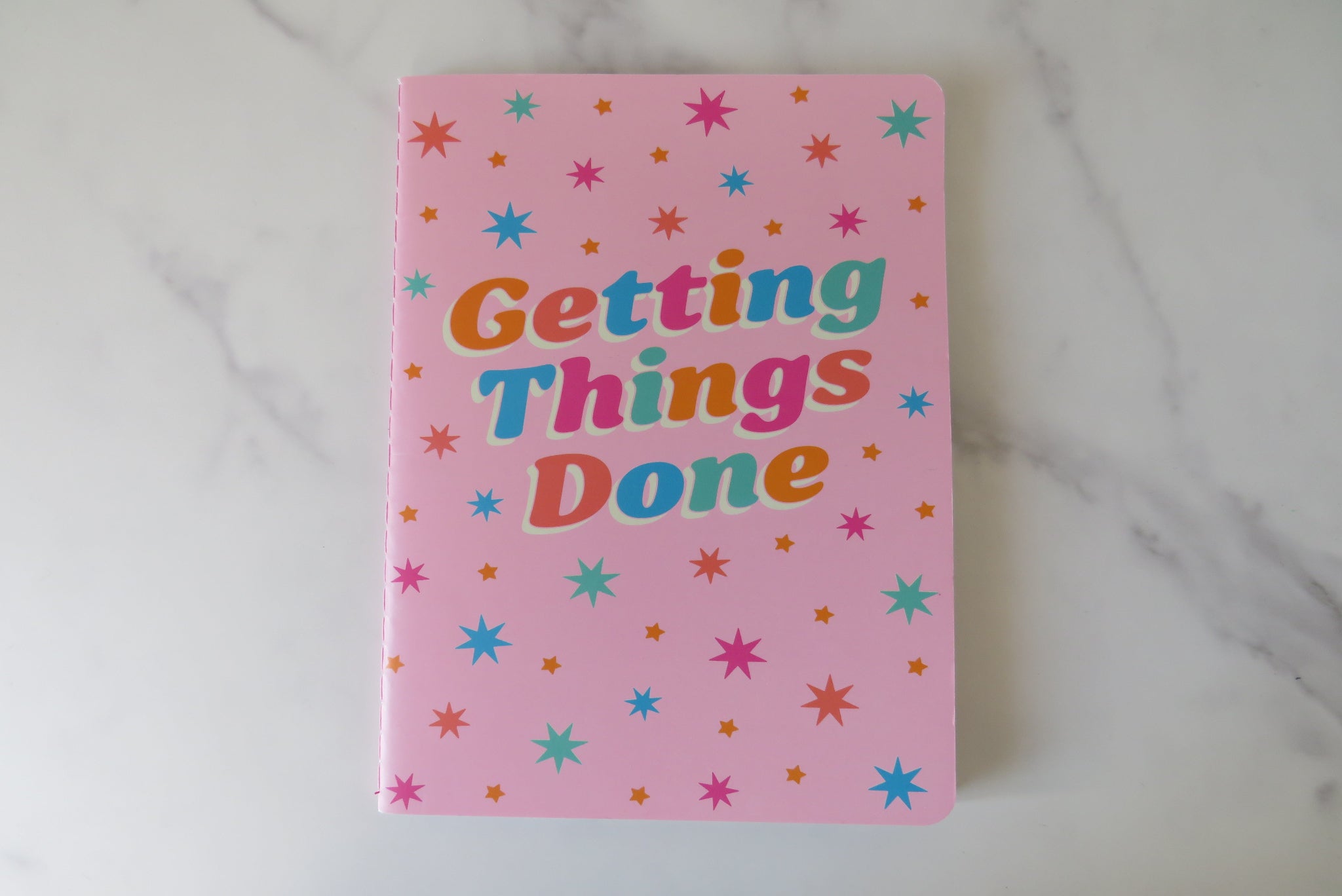 Pink notebook with 'Getting Things Done' text and star patterns on a marble surface.
