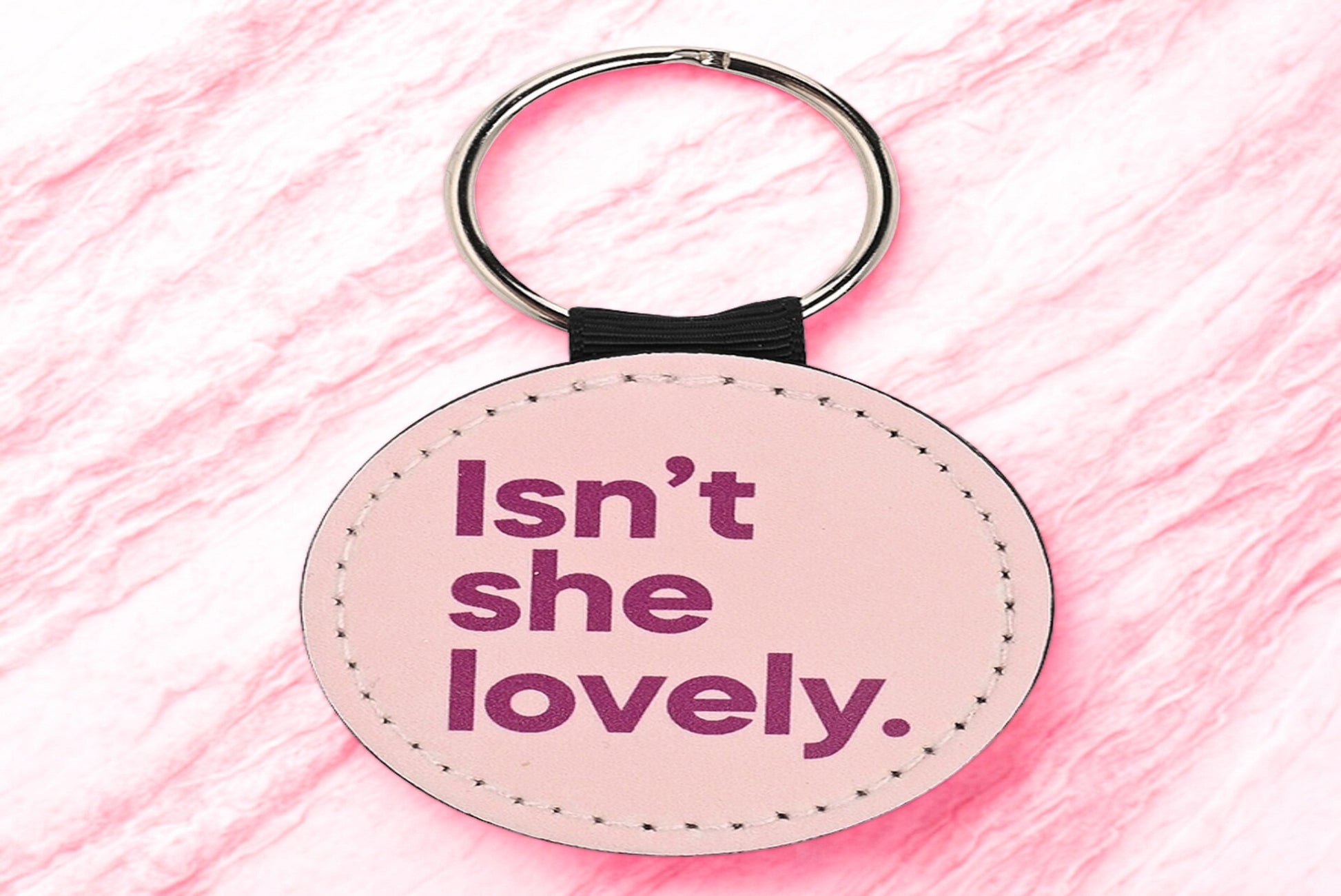 Round pink keychain with 'Isn't she lovely' text on a pink background