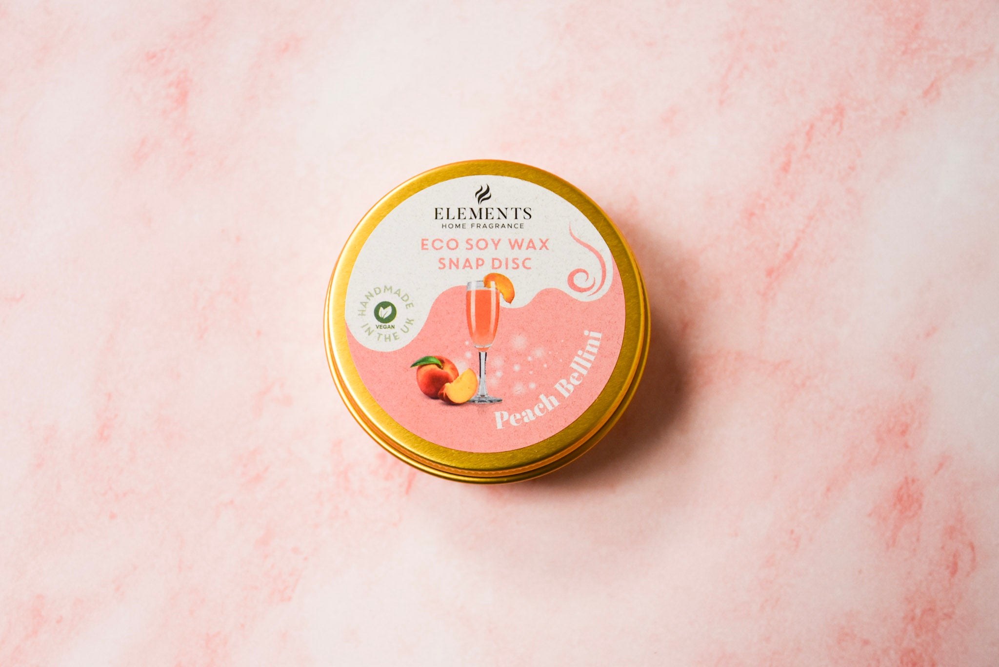 A round gold tin labelled 'Elements Home Fragrance Eco Soy Wax Snap Disc' in a Peach Bellini scent.