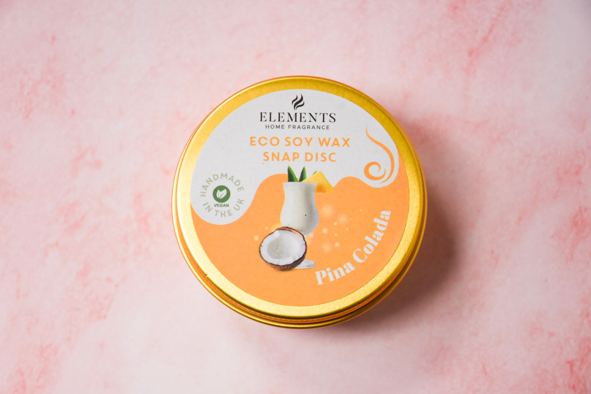 A round gold tin labelled 'Elements Home Fragrance Eco Soy Wax Snap Disc' in a Pina Colada scent.