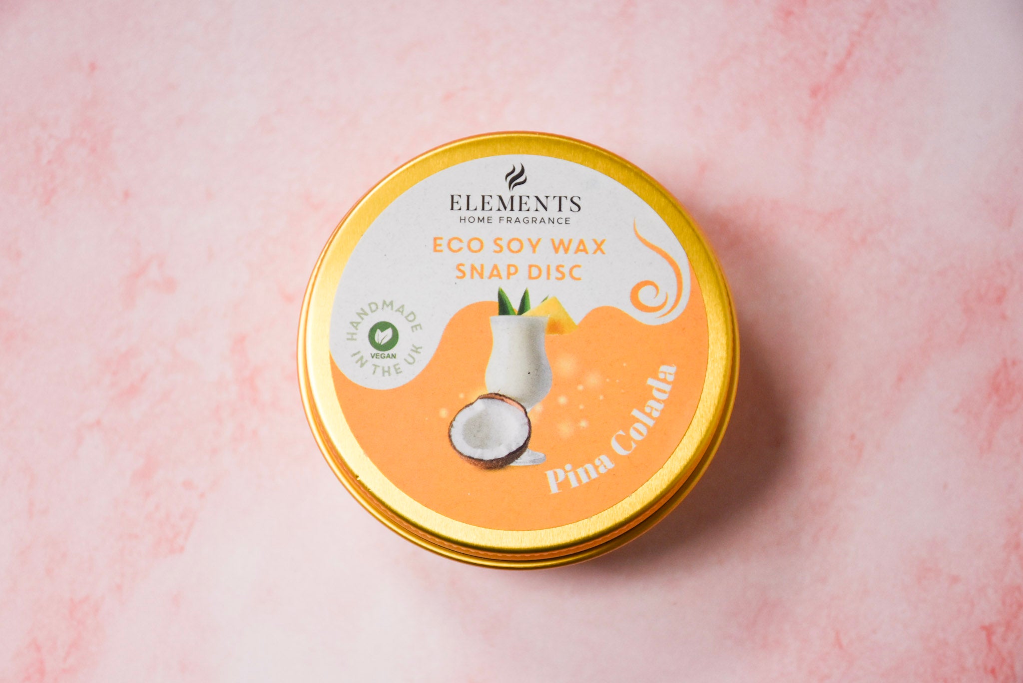 A round gold tin labelled 'Elements Home Fragrance Eco Soy Wax Snap Disc' in a Pina Colada scent.