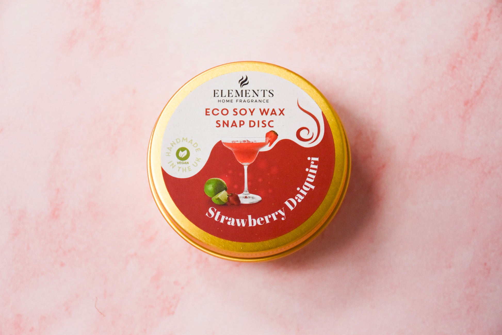 A round gold tin labelled 'Elements Home Fragrance Eco Soy Wax Snap Disc' in a Strawberry Daiquiri scent.