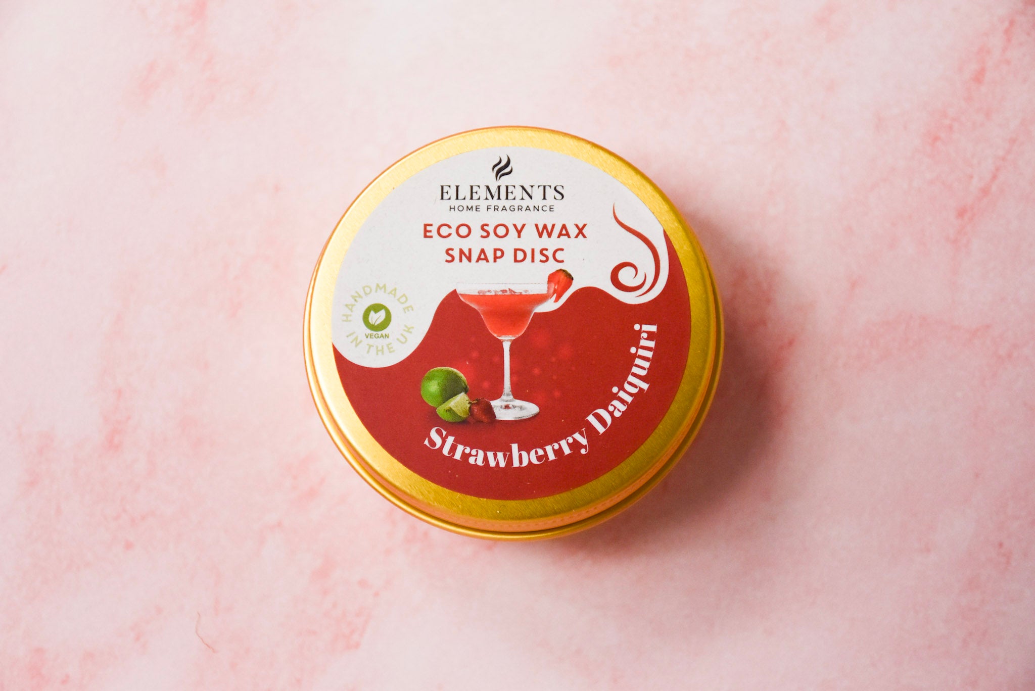 A round gold tin labelled 'Elements Home Fragrance Eco Soy Wax Snap Disc' in a Strawberry Daiquiri scent.
