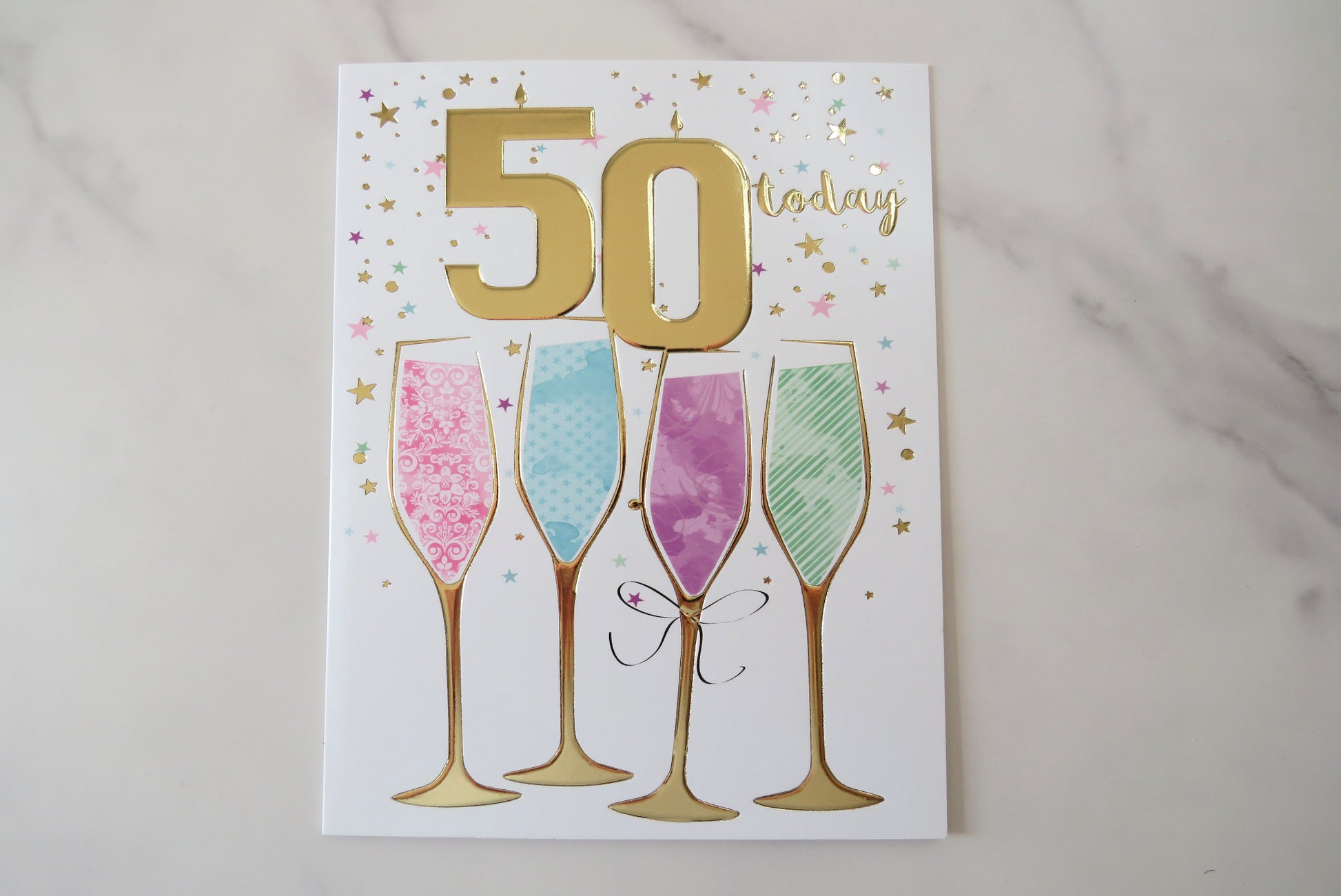 A 50th birthday card with colorful drink glasses and pink rose petals on a white background.