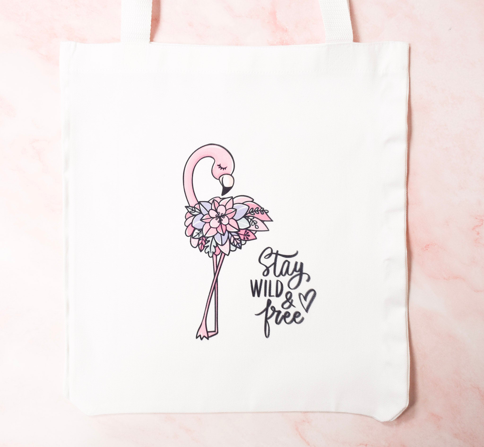 Floral flamingo design on a white tote bag with 'Stay Wild & Free' text.