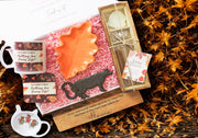 Collection of autumn-themed items including a mug, orange leaf-shaped trinket dish, warm vanilla incense set, black cow shaped bottle opener & highland cow tea tray.