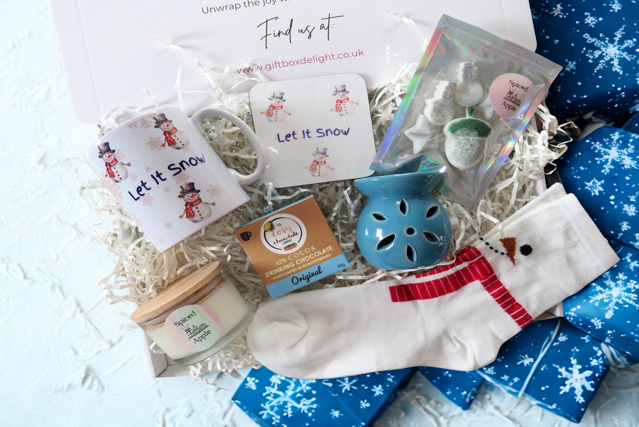 A christmas gift box with mug & coaster, hot chocolate, scented candles, scented wax melts, flower wax burner & snowman socks.