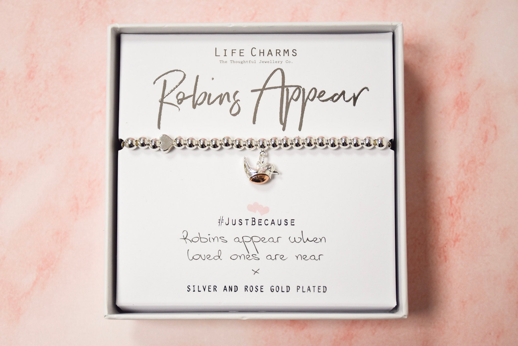 A bracelet with a silver and rose gold charm, presented in a box with the text 'LIFE CHARMS Robins Appear'.