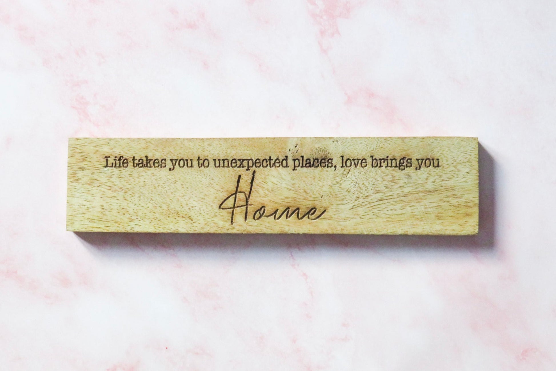Wooden home sign with engraved text Life takes you to unexpected places, love brings you Home.