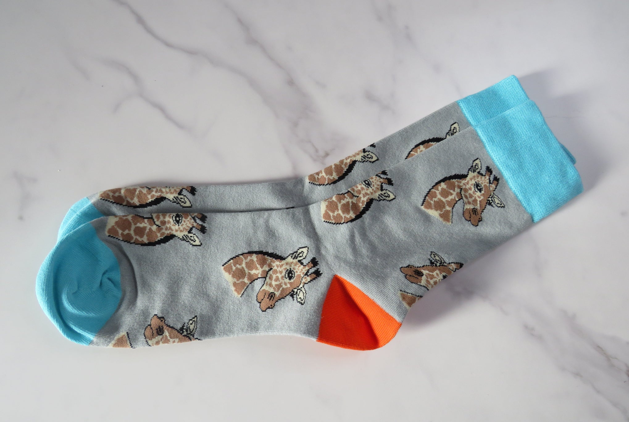 A pair of grey socks with giraffe patterns and blue trim.
