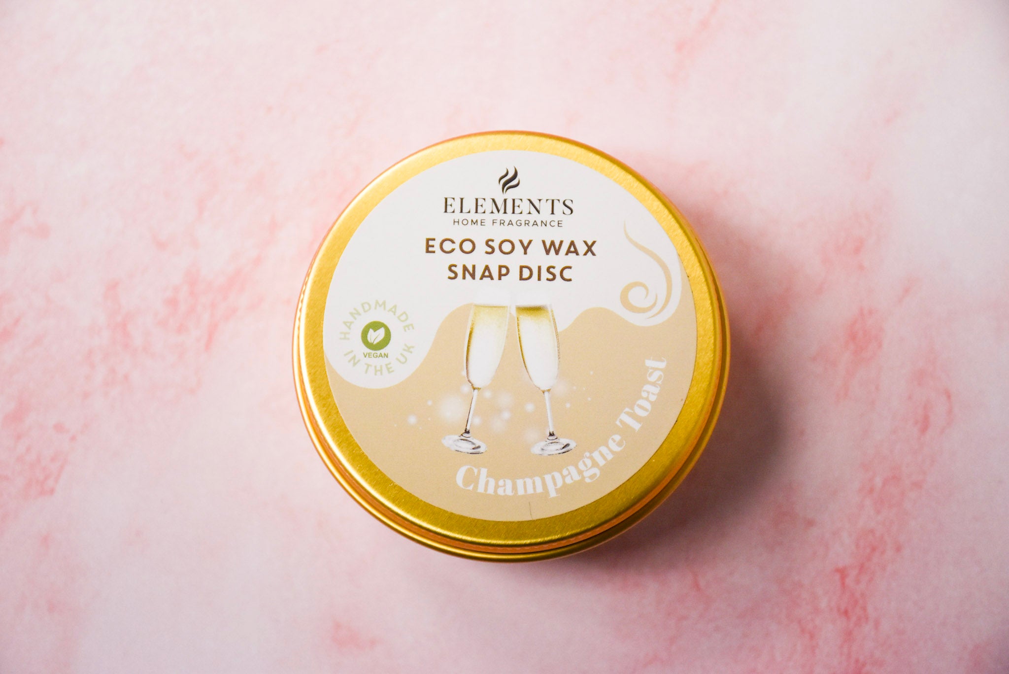 A round gold tin labelled 'Elements Home Fragrance Eco Soy Wax Snap Disc' in a Champagne Toast  scent.