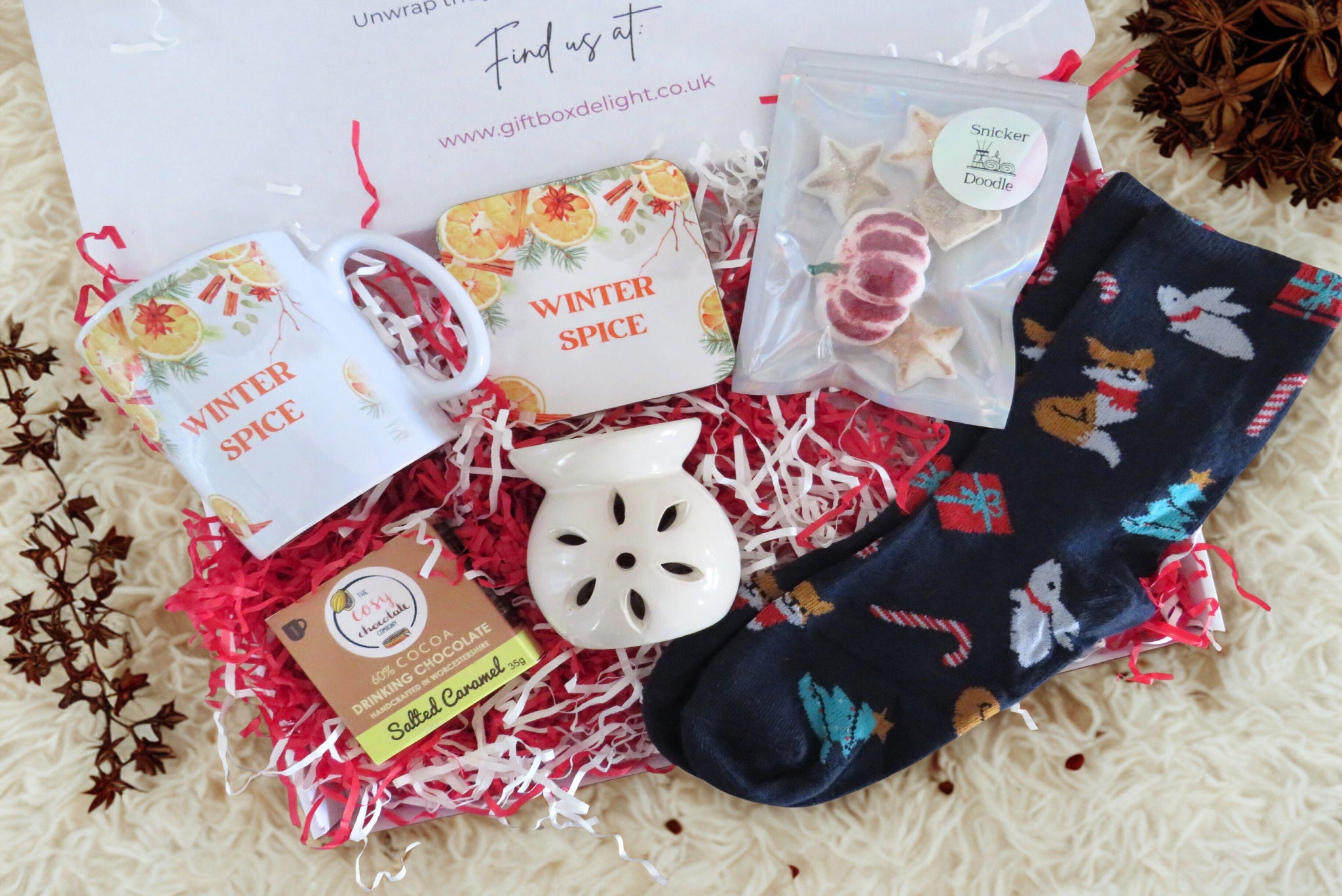 A christmas gift box with mug & coaster, salted caramel hot chocolate, flower wax burner, scented wax melts & blue christmas socks.